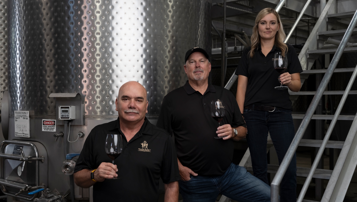 Three winemakers standing in front of equipment, each one holding a glass of wine