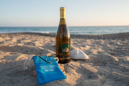 A bottle of Carneros Chardonnay on the beach alongside a black 4ocean x Frank Family custom bracelet and bag