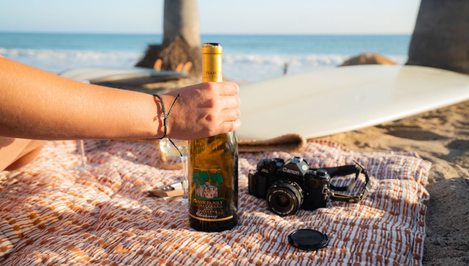 A bottle of Carneros Chardonnay on a beach blanket next to a surf board