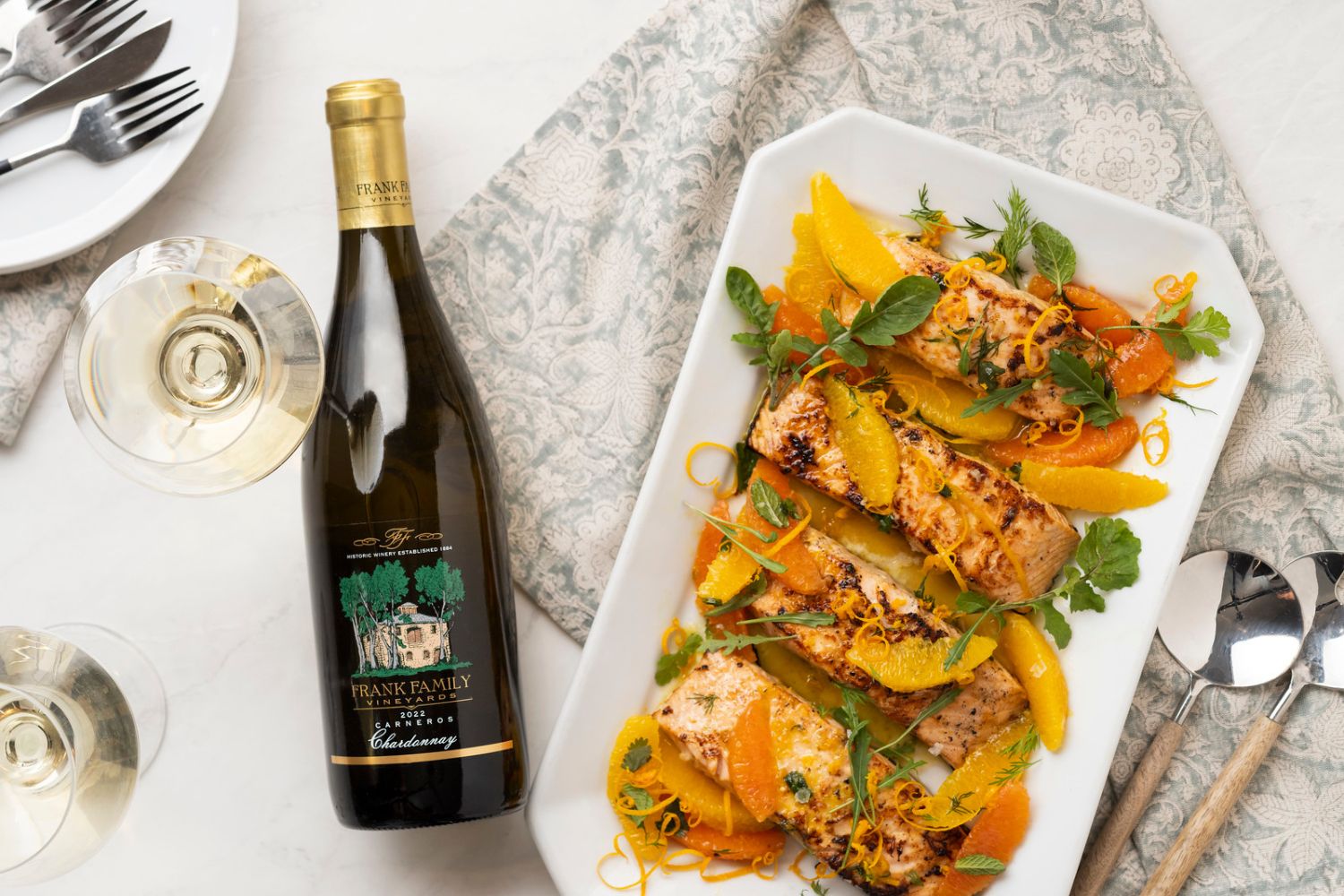 A bottle of Carneros Chardonnay beside a platter of salmon garnished with colorful citrus.