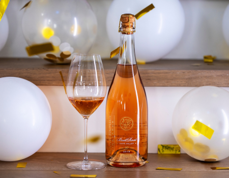 A bottle of Frank Family's 2019 Brut Rosé with confetti and balloons in the background. 