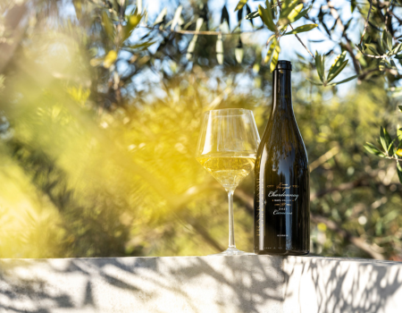 A bottle and glass of Frank Familys 2021 Lewis Vineyard Chardonnay with beautiful greenery in the background. 