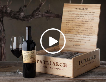 A bottle and wine glass are shown in front of a wood cellar box and trunk of a vine.